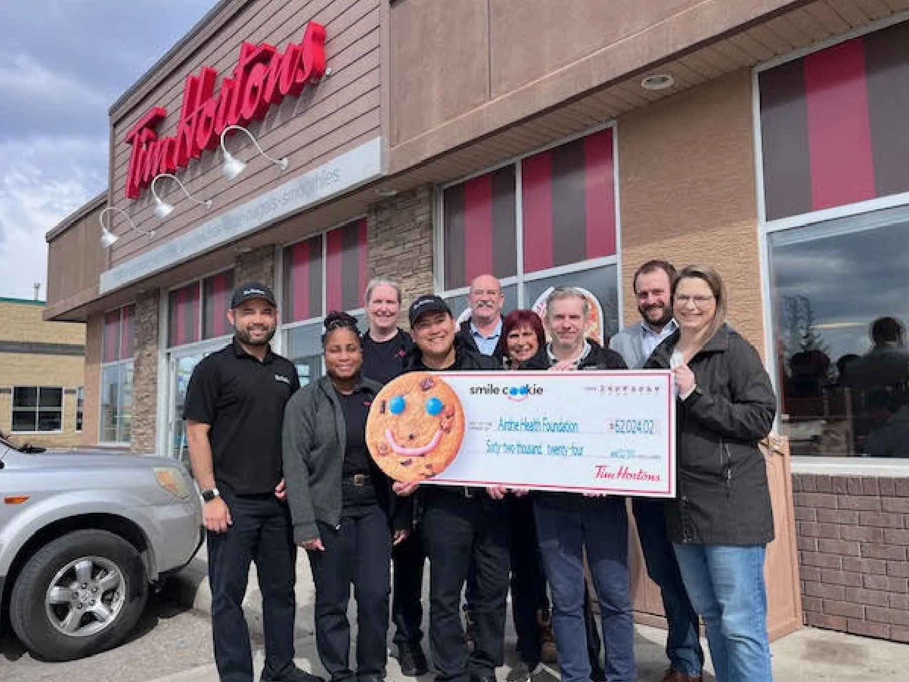 a group of people outside of Tim Hortons holding a big cheque from Tim Hortons as a donation to the Airdrie Health Foundation
