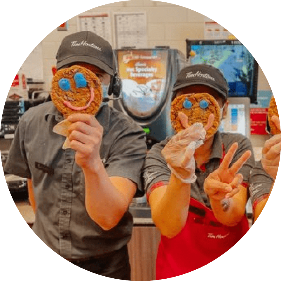 workers at Tim Hortons holding up smile cookies.