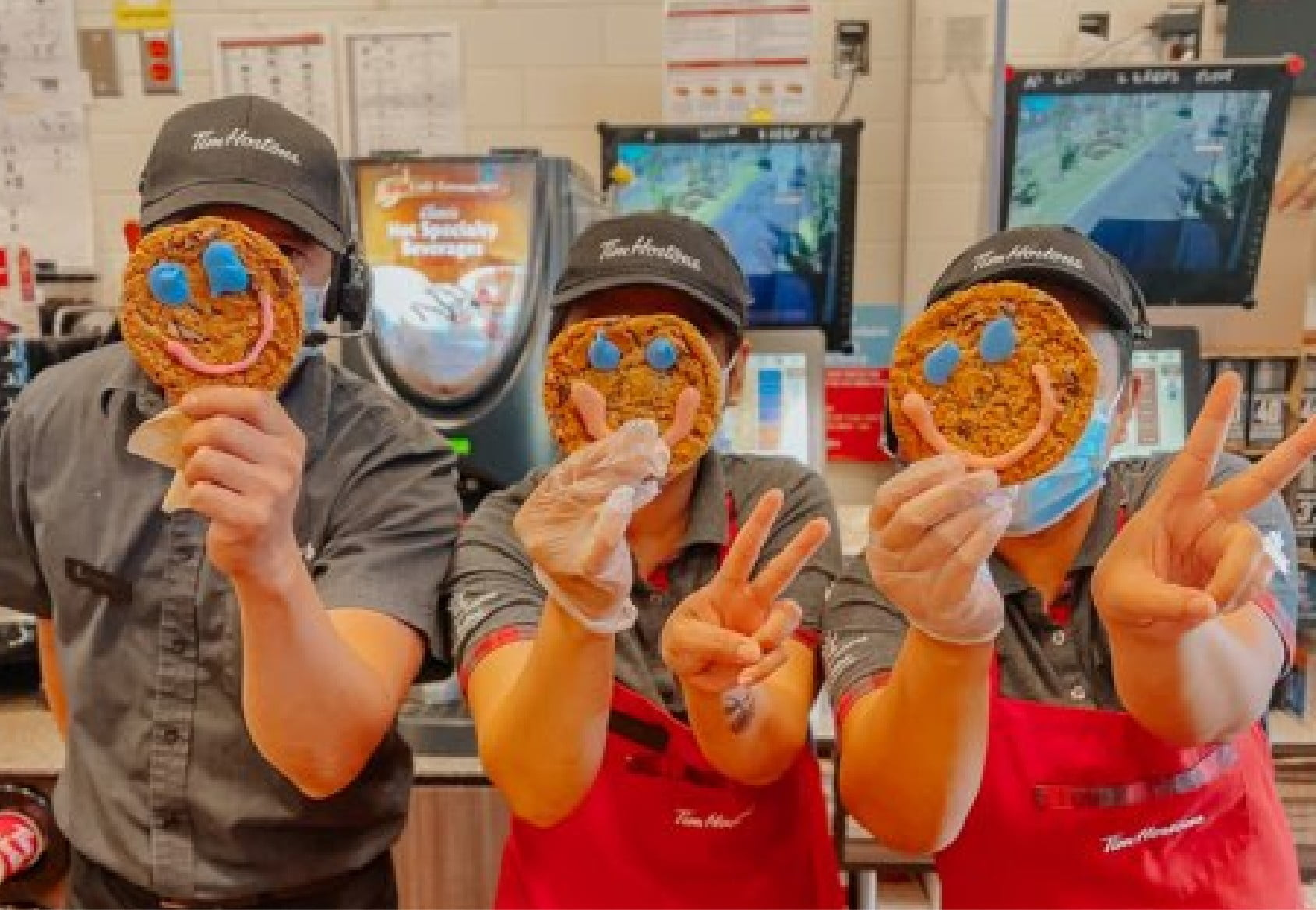 workers at Tim Hortons holding up smile cookies.